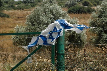 A torn and shredded blue and white flag of the State of Israel caught on a barbed wire fence.