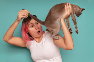 Surprised young woman looks under the tail of her pet cat