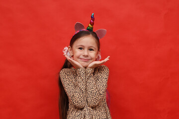 Portrait of a cheerful smiling little cute girl with a unicorn rim on a red background