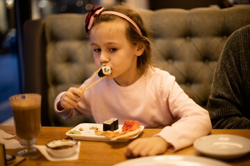 Cute little girl eating sushi in the cafe