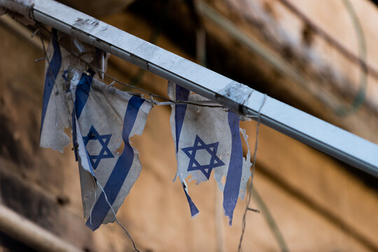 Two, small, weathered, torn, tattered and dirty blue and white flags of the State of Israel hanging on a railing outside a home in Israel.