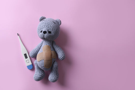 Toy bear with medical plasters and thermometer on pink background, flat lay. Space for text