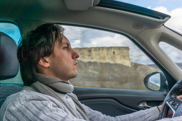 a young man, a brunette, a European, in a wool sweater, a driver behind the wheel of a car - a profile portrait against the background of a white rock in the window