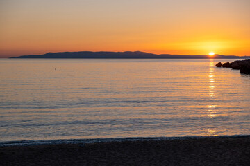 Sandy beach at sunset. Greece. Sundown over calm sea, reflection and orange color sky.