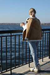 Lonely woman with cup of drink on pier near river, back view