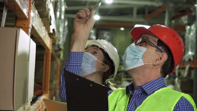 An elderly manager talks to a young female employee wearing masks and vests who works in the warehouse