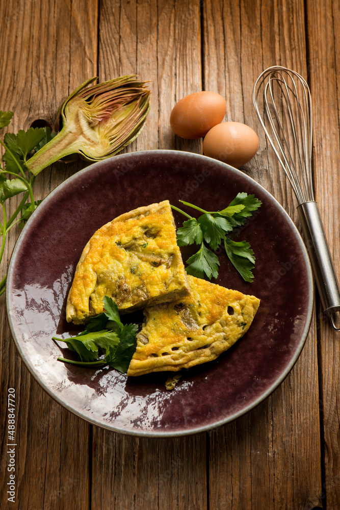 Poster slice omelet with artichoke over wooden table