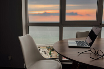 perfect freelance workspace with sea and sunset views. Laptop on a table in a room with a large window.