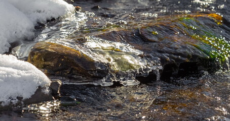 Flowing river water among snowdrifts in winter