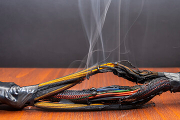 Burnt and melted wires smoke on a dark background. A short circuit in the twisted wires from the...