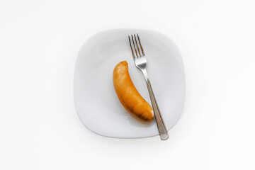 Chicken sausage and metal fork lying on white plate top view. Fast food concept.