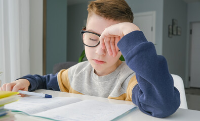 Naklejka na ściany i meble Bored and tired teenage boy doing homework on desk in his room
