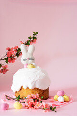 Fototapeta na wymiar Easter cake and colorful eggs and Easter decorative bunny on a pink background with spring cherry blossoms and copy space. Easter orthodox sweet bread.Easter card concept