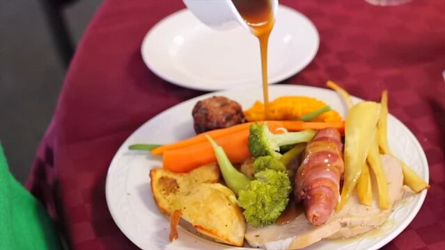 Roast Christmas dinner with turkey, pork, pigs in blankets, roast potatoes, parsnips, stuffing ball, carrots, broccoli and gravy carvery. Slow motion pouring gravy. 