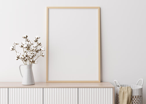 Empty vertical picture frame on white wall in modern living room. Mock up interior in minimalist, scandinavian style. Free space for picture. Console, rattan basket, cotton plant in vase. 3D rendering