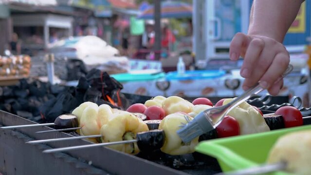 Juicy Kebabs from Grilled Vegetables are Cooked on Grill Outdoors. Male hand greases surface of vegetables with oil and marinade before frying. Preparing peppers, tomatoes. Street kitchen. Market.