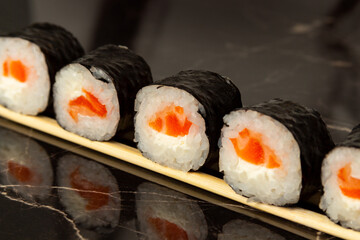 Sushi rolls with salmon, lie on wooden sticks on a dark background