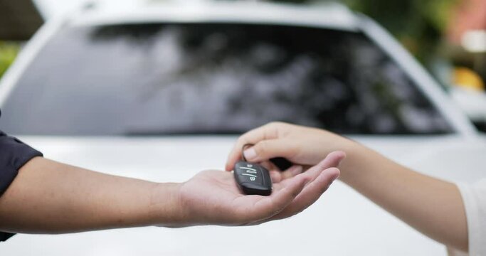 Close up of a woman handing over a car key to a mechanic man with blurred white car background. Car service concept.