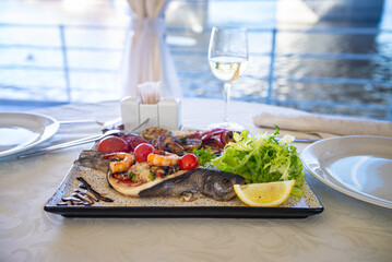 baked trout with grilled vegetables and shrimp and fresh lettuce on a white plate, food and delicacies
