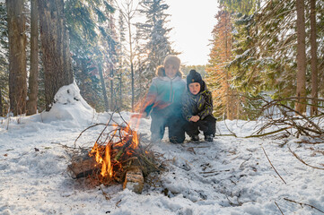 A woman with a boy by a campfire in winter in the forest . - 488852588