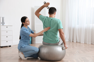 Orthopedist helping patient to do exercise with dumbbells in clinic. Scoliosis treatment - obrazy, fototapety, plakaty