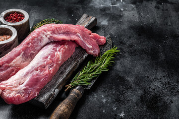 Tenderloin pork raw meat, uncooked fillet on wooden board with herbs. Black background. Top view. Copy space