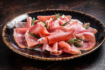 Slices of prosciutto crudo parma or jamon serrano with rosemary. Dark background. Top view