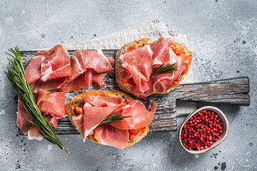 Spanish Tapas - Toast with tomatoes and cured Slices of jamon iberico ham on wooden board. Gray background. Top view