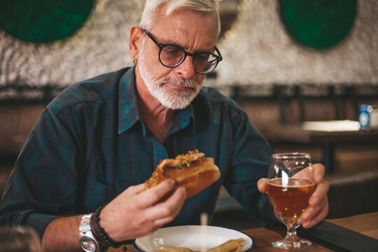 An adult man is having lunch in a pub. Eating a burger with beer.