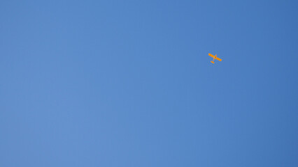 Light aircraft flies in the clear blue sky. Wallpaper or background. Yellow small plane. General aviation. Air sports and tourism