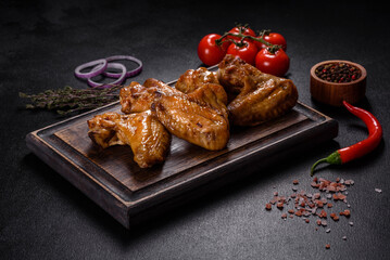 Baked chicken wings with vegetables and spices on a black background