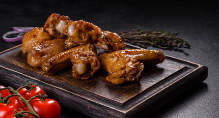 Baked chicken wings with vegetables and spices on a black background