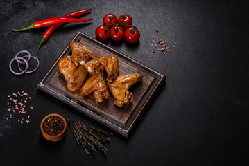 Obraz na płótnie Canvas Baked chicken wings with vegetables and spices on a black background