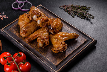 Baked chicken wings with vegetables and spices on a black background