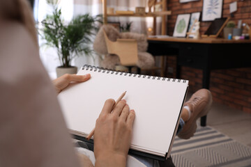 Woman drawing in sketchbook with pencil at home, closeup