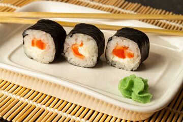Sushi rolls with salmon lie on a white dish and a bamboo mat