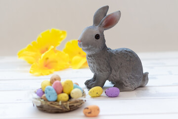 happy Easter, colorful Easter eggs in a nest and a rabbit on a white wooden background. Easter decoration