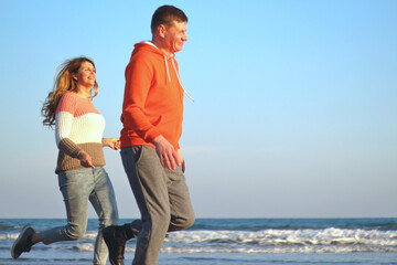 middle age husband and wife are jogging on a beach and smiling