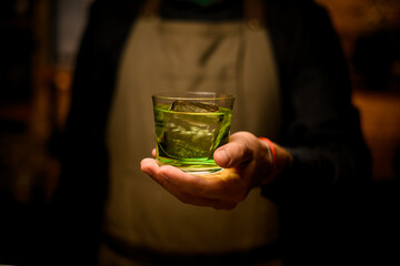 front view of glass with a green drink on the hand of a male bartender