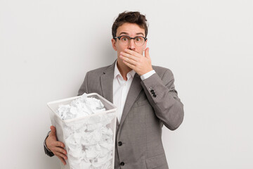 young handsome man covering mouth with hands with a shocked. paper balls basket concept