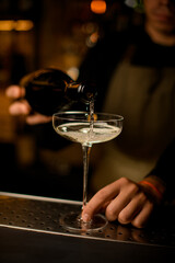 close-up of wine glass into which a drink is poured from a bottle