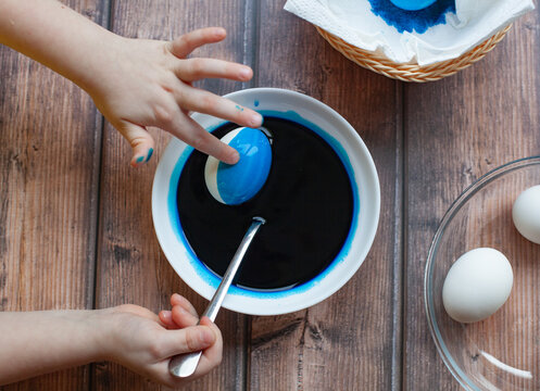 girl in a plate with paint paints an egg blue, Easter