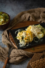 A casserole with baked fish and cheeze sauce on the dark background, potatoes in a clay bowl