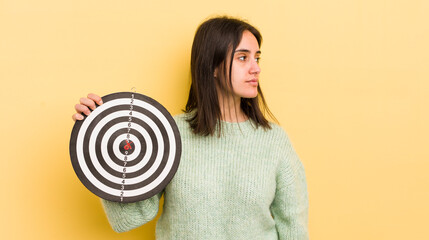 young hispanic woman on profile view thinking, imagining or daydreaming. darts target concept