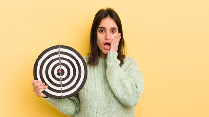 young hispanic woman feeling shocked and scared. darts target concept