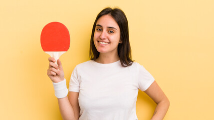 young hispanic woman smiling happily with a hand on hip and confident. ping pong concept