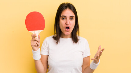 young hispanic woman feeling extremely shocked and surprised. ping pong concept