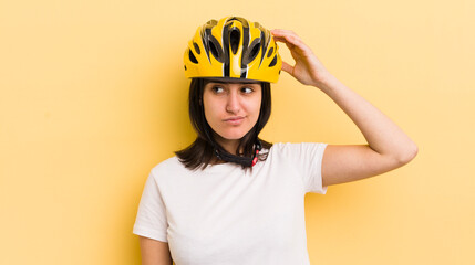 young hispanic woman smiling happily and daydreaming or doubting. bike helmet concept