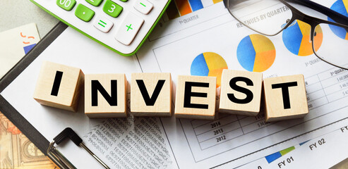 The inscription on the cubes, the word INVEST on the cubes of wooden texture. View from above. Desktop with documents. An inscription on a financial, business or economic theme.