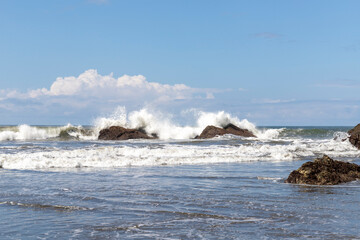 Rock on the beach of the ocean with waves and cloudy skies